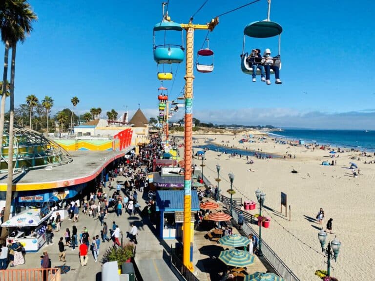 Santa Cruz beach with golden sand, beachgoers enjoying the sun and surf, the iconic boardwalk and amusement rides.