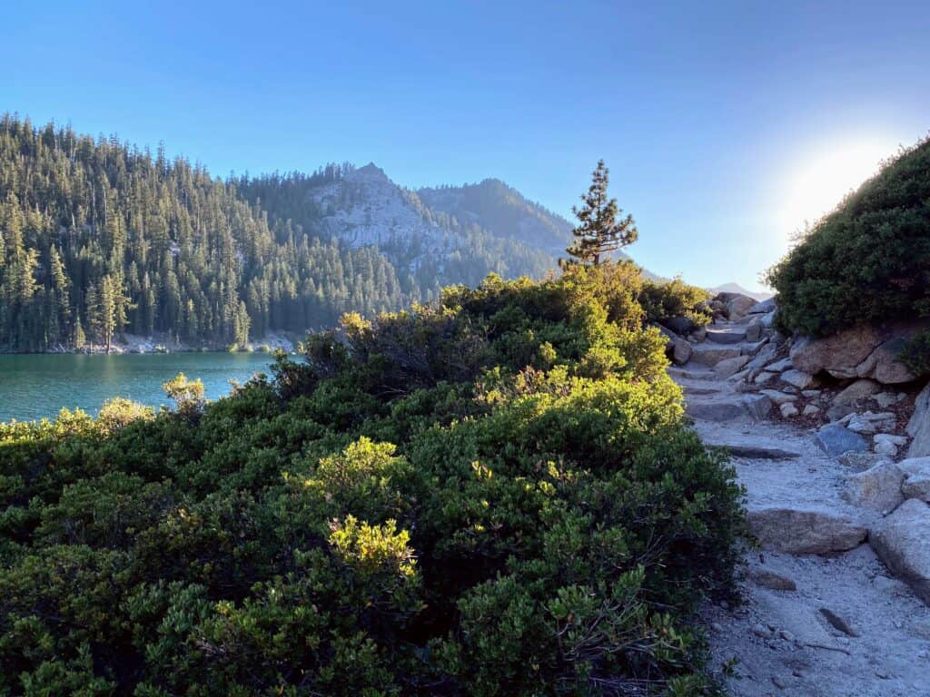A rocky terrain hiking trail next to a blue lake and mountain scenery