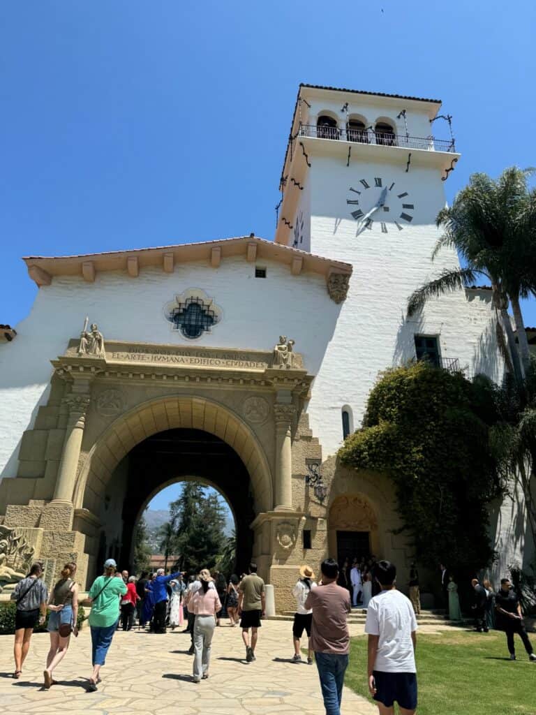 The entrance gate of the Santa Barbara Courthouse, showcasing the ornate archway and part of the clock tower above it. The Spanish Colonial Revival details are highlighted against a clear blue sky, emphasizing the building's historic charm.