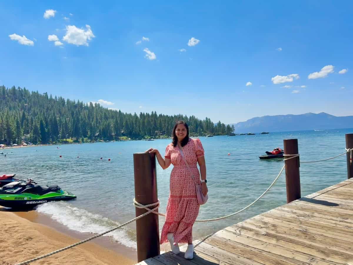 A girl in a red maxi dress posing on a boardwalk with a blue lake and green hills in the backdrop