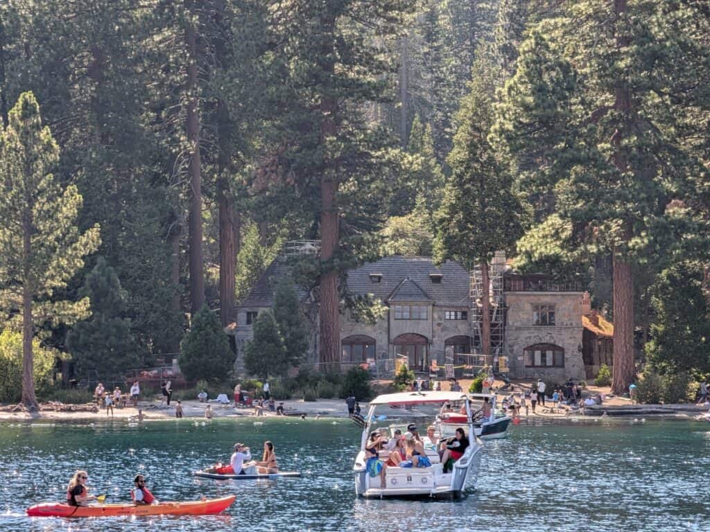 People enjoying water activities near a beach with a castle and hills in the backdrop