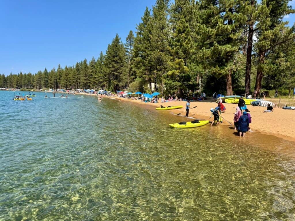 A lakeside beach with clear water and people kayaking