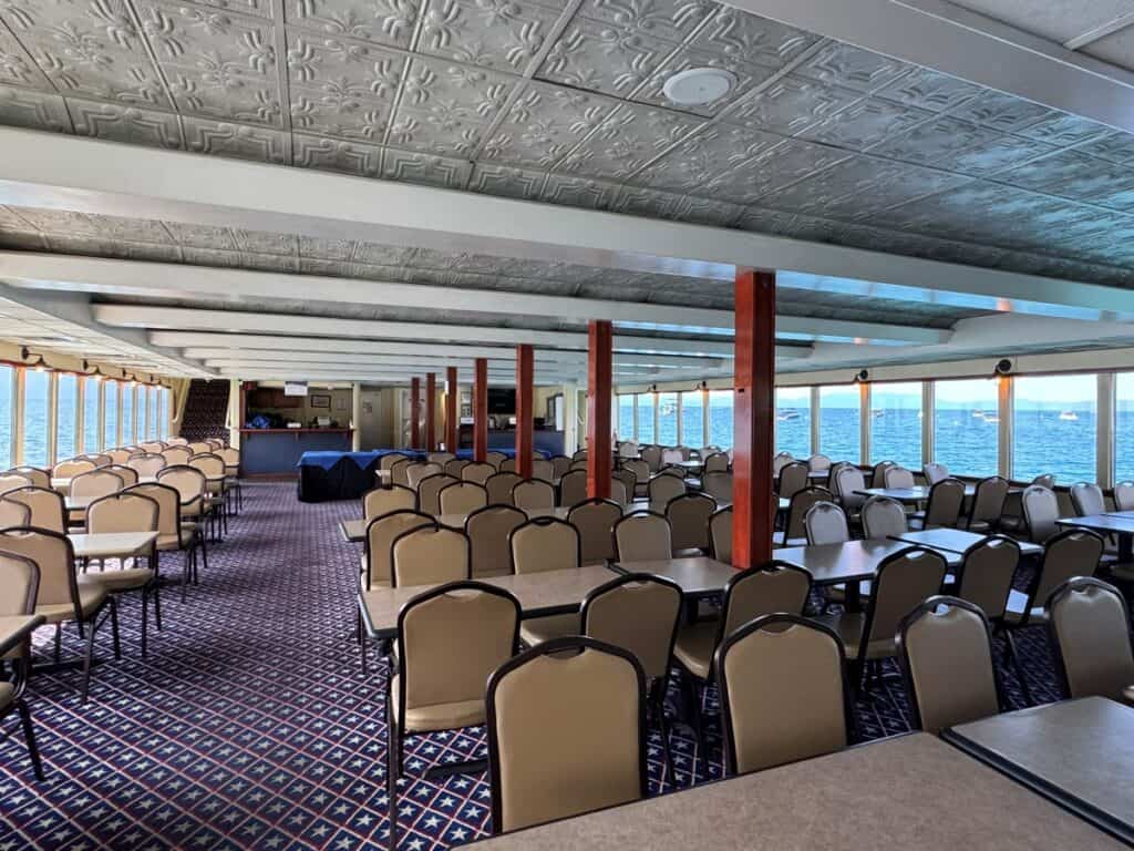 An enclosed seating area on a boat with tables, chairs and large windows