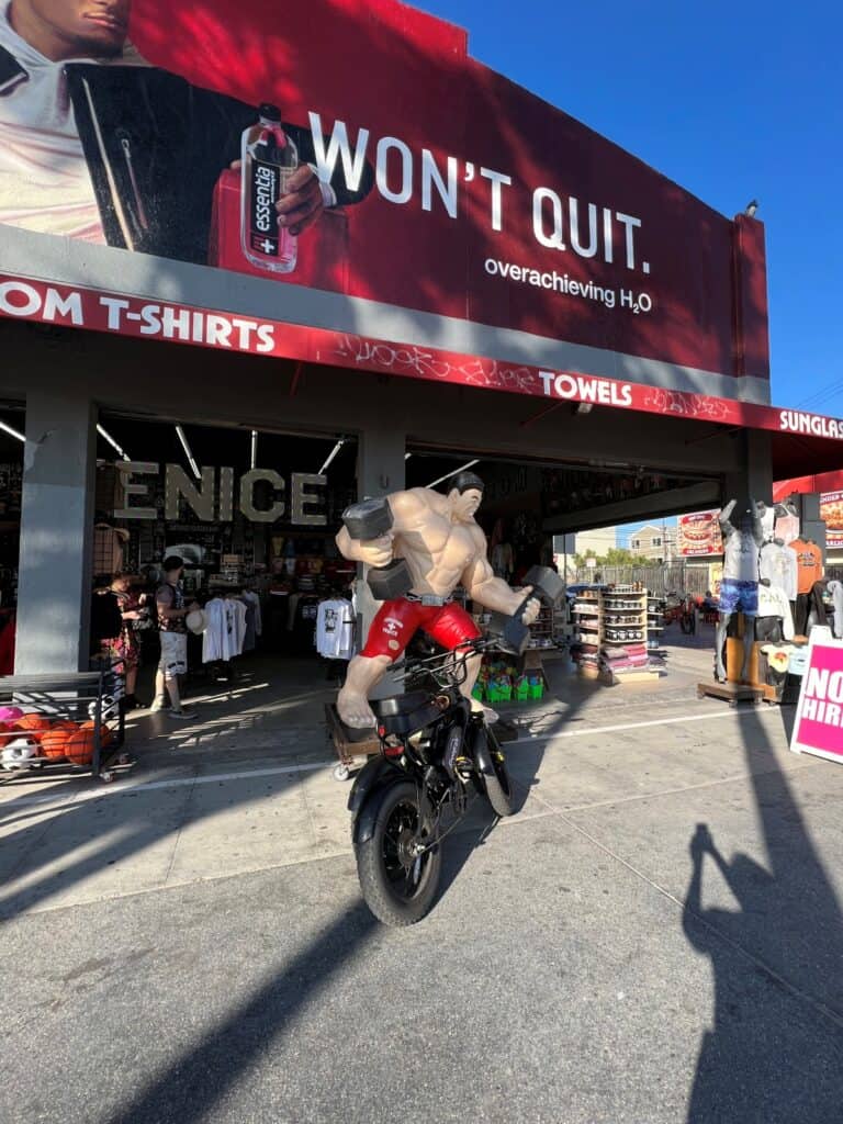 A souvenir shop at Venice beach with a statue of a muscular man on a bike lifting weights