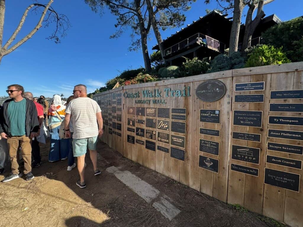 a busy dirt trail with a wall that reads Coast Walk trail